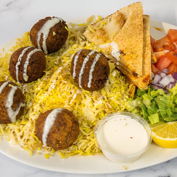 Falafel plate with yellow rice, pita bread, salad, and a side of white sauce and lemon.