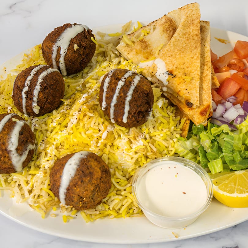Falafel plate with yellow rice, pita bread, salad, and a side of white sauce and lemon.