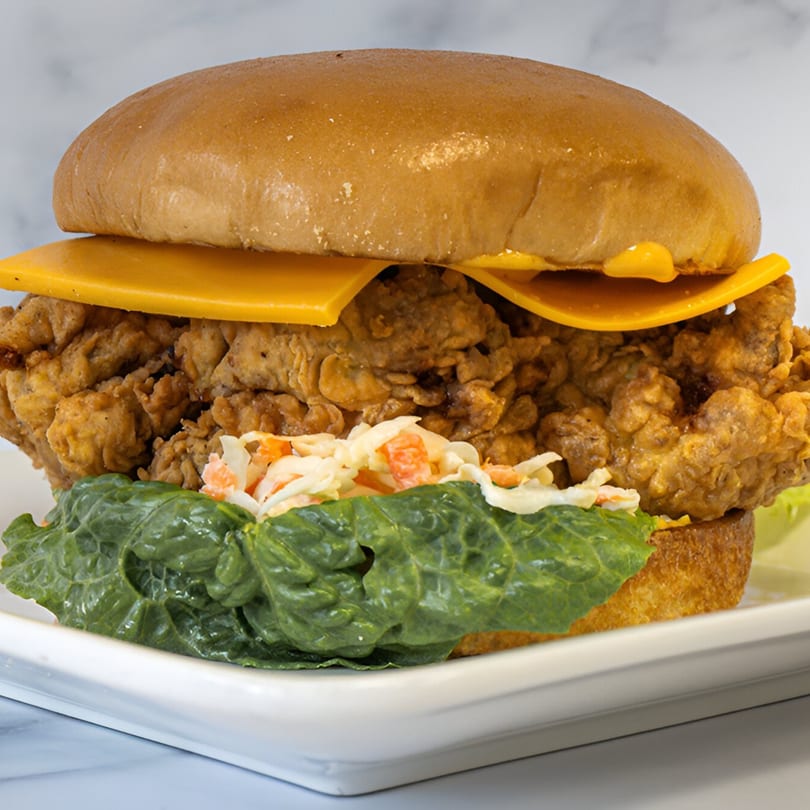 A crispy fried chicken sandwich with melted cheese, coleslaw, and lettuce on a bun.