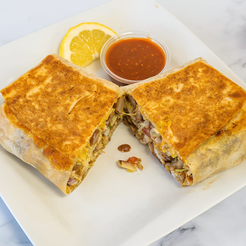 A grilled shawarma wrap, cut in half, revealing its savory filling, with a lemon wedge and sauce.