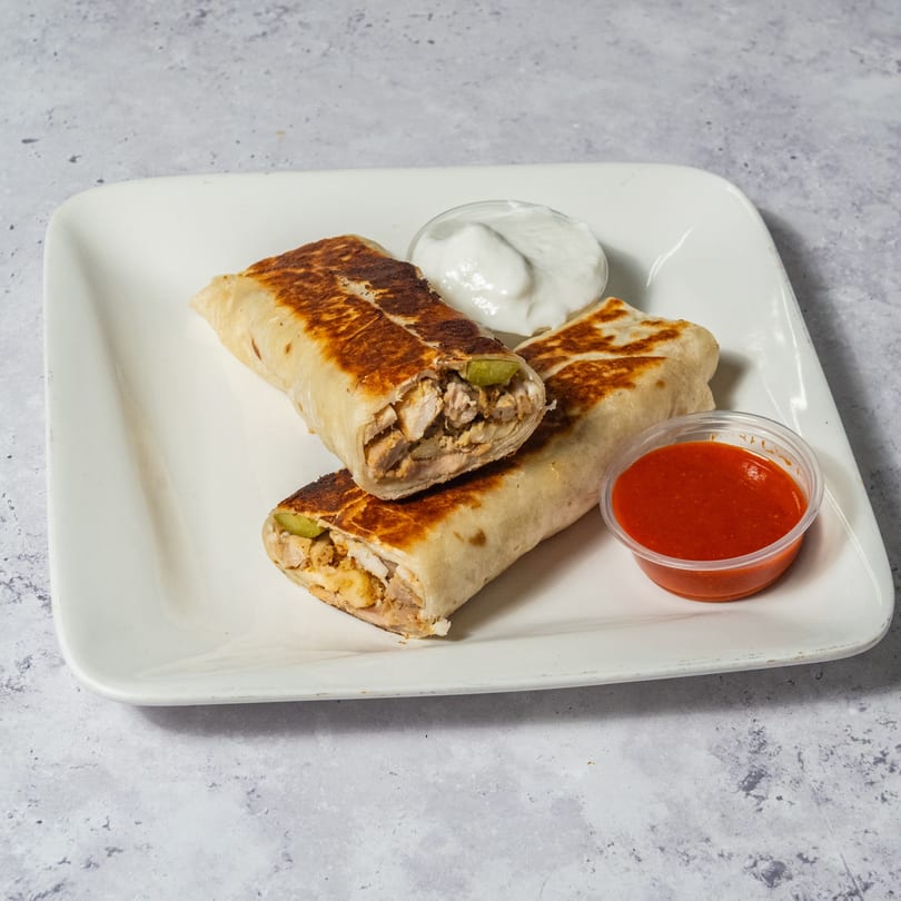 Two grilled chicken shawarma wraps with white sauce and red chili sauce on a white plate.
