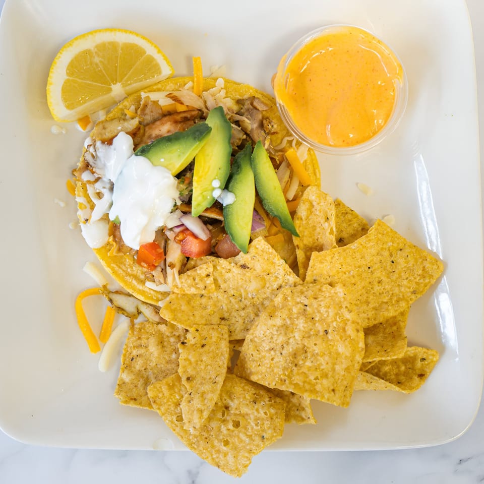 Shawarma taco with avocado, sour cream, and a side of tortilla chips and dipping sauce.