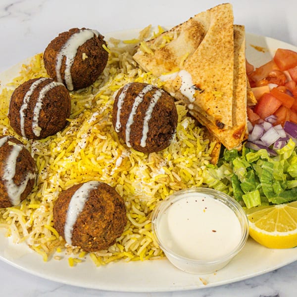 A Shawarma Azmi falafel plate with rice, pita, salad, and a side of sauce.