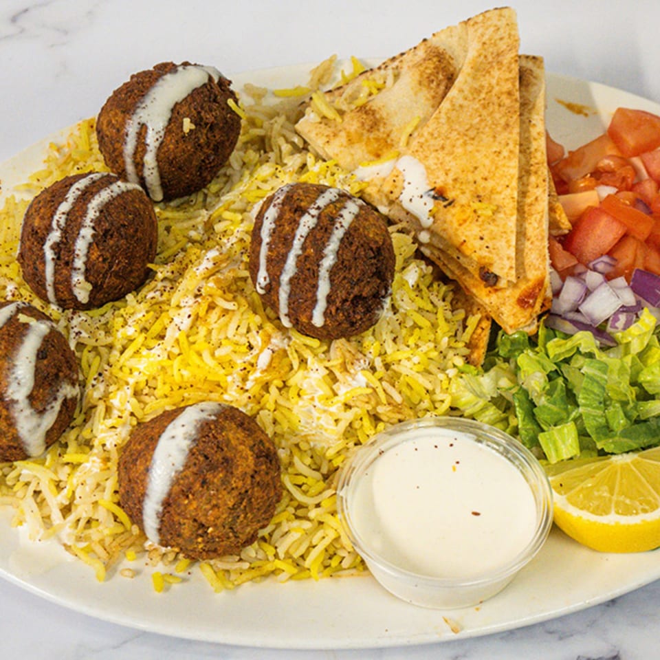 A Shawarma Azmi falafel plate with rice, pita, salad, and a side of sauce.